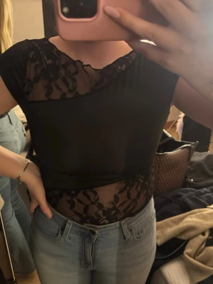 Svart topp med spetsdetaljer🙌 - Snygg svart topp med genomskinliga spetsdetaljer upptill och vid midjan. Kortärmad och figurnära passform! Köpt på Vinted och inga prislappar är kvar därav vet jag ej storlek (skulle gissa på S) eller vart den är ifrån, säljer på grund av att den var för liten för mig☺️