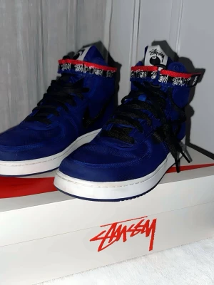 Nike x Stussy blåa high sneakers - Unika blåa high-top sneakers från Nike i samarbete med Stussy. Skorna har svarta skosnören, vit sula och detaljer i rött och vitt runt ankeln. Materialet är en mix av textil och syntet. Stussy-logga syns på plösen och runt kragen för extra streetwear-vibe. Finns också extra snören och en till carbor band sak  PRISET ÄR INTE HUGGET I STEN !     Nypris : 2499                                    Tar även byten !