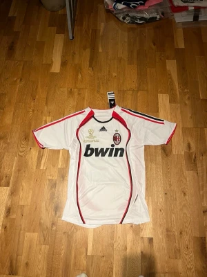 Ac Milan 06/07 away kit X Kaka 22 - Säljer en vit AC Milan bortatröja från Adidas med Kaka och nummer 22 på ryggen. Tröjan har röda och svarta detaljer, Bwin som sponsor på bröstet och klubbmärke samt Adidas-logga fram. Tillverkad i lätt och ventilerande material, perfekt för fotboll.