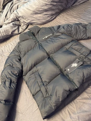 Svart pufferjacka från Sixth June - Säljer en svart pufferjacka från sail racing med hög krage och dragkedja framtill. Jackan har två stora fickor på sidorna och logga på bröstet samt en detalj på ryggen. Perfekt för kalla vinterdagar och riktigt trendig look.