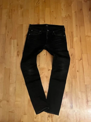 Svarta slim fit jeans från Lee - Snygga svarta slim fit jeans från Lee med klassisk femficksmodell och diskreta slitningar. Jeansen har smal passform och är tillverkade i ett stretchigt denimtyg för extra komfort. Perfekta för en trendig och avslappnad stil.