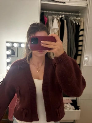 Vinröd kofta med rosetter - Fin stickad kofta från bikbok i jätte mjukt material med små rosetter på! Storlek XS-S och endast använd en gång!!