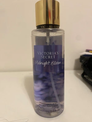 Victoria's Secret Midnight Bloom mist - Fräsch body mist från Victoria's Secret i doften Midnight Bloom. Flaskan är genomskinlig med lila etikett och har ett elegant guldigt lock. Rymmer 250 ml och har en modern, rund form. Perfekt för dig som gillar blommiga och fräscha dofter.