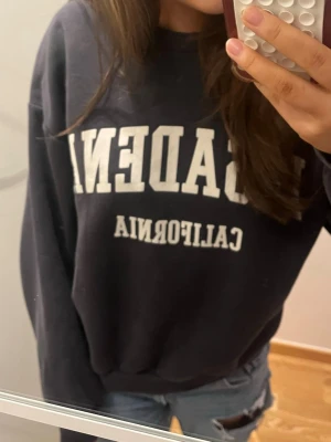 Sweatshirt / collagetröja  - Collegeinspirerad mörkblå sweatshirt med vit text 'ACADEMY CALIFORNIA' på bröstet. Tröjan har rund halsringning och långa ärmar. Perfekt för en avslappnad och trendig look.