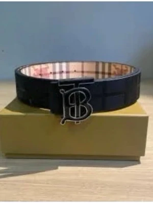 Letar efter en Svart Burberry bälte med TB-spänne - Letar efter en Snyggt svart bälte från Burberry med klassiskt TB-monogram i metall som spänne. Insidan har det ikoniska randiga Burberry-mönstret i beige, rött och svart. Perfekt accessoar för att lyfta din outfit.