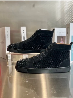 Svarta Louboutin sneakers med nitar - Säljer ett par svarta sneakers från Christian Louboutin med coola svarta nitar över hela ovandelen och den ikoniska röda sulan. Skorna har en hög siluett, snörning och är tillverkade i mocka och läder. Perfekta för dig som vill sticka ut med din stil.