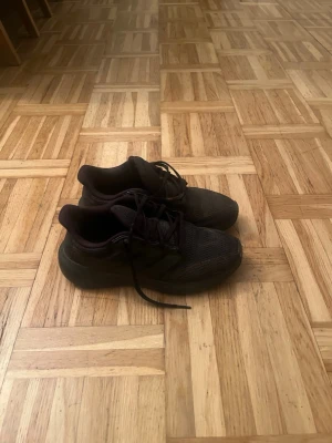 Svarta Adidas sneakers i mesh - Säljer ett par helsvarta Adidas sneakers med lågt skaft och klassiska tre ränder på sidan. Ovandelen är i ventilerande meshmaterial och sulan är i gummi. Skorna har snörning och en sportig, clean look som passar till det mesta.