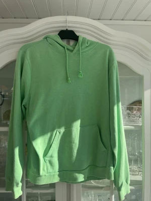 Grön hoodie från SOC med ficka - Snygg grön hoodie från SOC med klassisk känguruficka och dragsko i huvan. Tillverkad i mjukt material som känns sköntu mot huden. Perfekt för chill dagar eller när du vill ha en avslappnad stil. Långa ärmar och ribbade muddar för extra komfort.