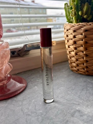 Synchrony från Björk and berries  - En stilren parfym från Björk and berries, Synchrony i en smal, genomskinlig glasflaska med vinrött lock. Flaskan har enkel och modern design med texten tryckt i svart. Perfekt att ha med i väskan för en fräsch doft när som helst.  Roll on parfym 10ml. Ny