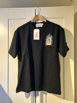 Svart Casablanca t-shirt med tryck - Svart t-shirt från Casablanca med färgglatt tryck fram och stort grafiskt tryck på ryggen med texten 'Avenida Casablanca'. Klassisk passform och rund hals. Perfekt för dig som vill ha en stilren men ändå unik look.