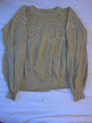 Smuts-gul stickad tröja från KappAhl - Stickad smuts-gul tröja från KappAhl med rund halsringning och ett snyggt hålmönster över bröstet och axlarna. Tröjan har långa ärmar och ribbade muddar vid ärmslut och nederkant. Perfekt för lager på lager och en avslappnad stil.