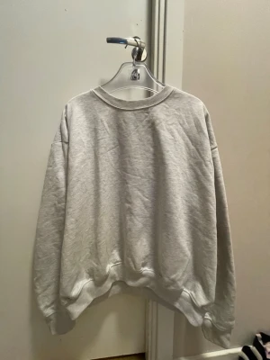 Grå sweatshirt från 157 - En basic grå sweatshirt från 157 med rund halsringning och ribbade muddar vid ärmslut och nederkant. Tillverkad i mjukt material som känns skönt mot huden. Perfekt för en avslappnad och stilren look.