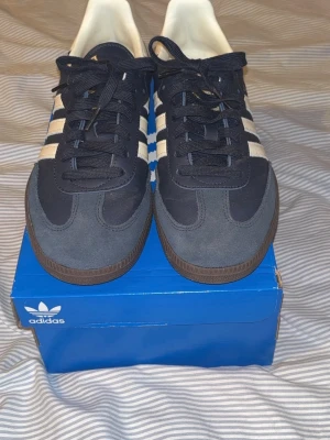 Adidas Samba OG mörk blåa/vit sneakers - Klassiska Adidas Samba OG sneakers i mörkblå mocka och läder med vita detaljer och bruna gummisulor. Bara använd 1 gång på grund av att storleken var för liten. Priset är ej hugget i sten nypris 1500