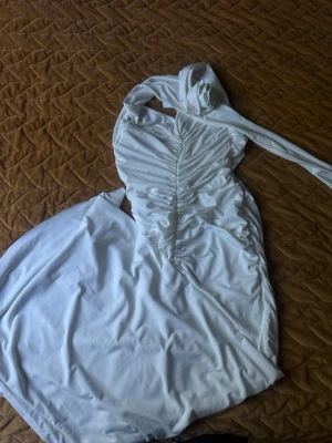 Jätte fin vit långklänning med drapering från EYYO ATELIER - Elegant vit långklänning med draperad effekt längs sidorna och en axelbandslös design. Klänningen har en asymmetrisk axel med tygdetalj som kan knytas och ger en unik look. Perfekt för dig som vill sticka ut med en stilren och modern klänning. Helt ny med lapp