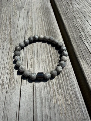 Grått armband med marmorerade pärlor - Snyggt armband med runda, marmorerade pärlor i olika grå toner och en metallisk detalj. Pärlorna har en naturlig stenlook och armbandet är elastiskt för enkel användning. Perfekt accessoar för en stilren och modern vibe.
