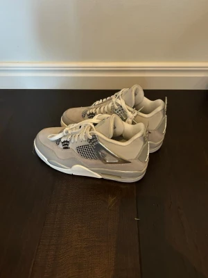 Nike Air Jordan 4 vit/grå sneakers oanvända 43 - Snygga Air Jordan 4 sneakers från Nike i vitt och ljusgrått med detaljer i silver. Skorna har meshpaneler på sidorna, klassisk snörning och synlig Air-enhet i sulan. Materialmix av mocka, läder och mesh ger en modern och clean look.