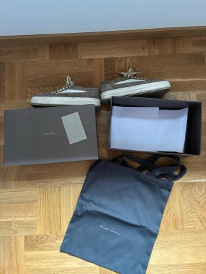 Rick Owens- Vans - Säljer ett par grå sneakers från Rick Owens med vit sula och vita detaljer. Skorna har klassisk låg profil, snörning och är tillverkade i mocka. Medföljer originalkartong och dustbag. Perfekta för dig som gillar stilrena och exklusiva sneakers.