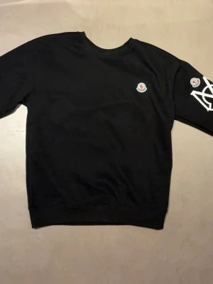 Svart Moncler t-shirt med logga - Snygg svart t-shirt från Moncler med stor vit logga och klassisk Moncler-patch på bröstet. T-shirten har rund hals och är tillverkad i mjuk bomull för en bekväm känsla. Perfekt för dig som gillar exklusiva streetwear-plagg.