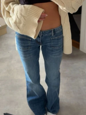 Blå bootcut jeans med låg midja - Säljer ett par blå bootcut jeans med låg midja och klassiska fickor fram. Jeansen har en avslappnad passform och är perfekta för en trendig vardagslook. Materialet är denim i bomull och färgen är mellanblå tvätt.