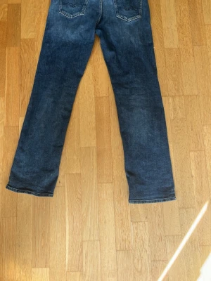 Blå  raka replay jeans med slitningar - Säljer ett par klassiska blå jeans med raka ben och snygga slitningar framtill. Jeansen har fem fickor och kontrastsömmar. Perfekta för en avslappnad och trendig look. Priset kan diskuteras med ett snabbt köp