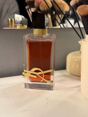 Yves Saint Laurent Libre EdP 90ml - Säljer en ikonisk parfym från Yves Saint Laurent, Libre Eau de Parfum. Flaskan är i genomskinligt glas med guldiga detaljer och svart lock. Doften är elegant och modern, perfekt för dig som vill sticka ut. Flaskan rymmer 90 ml och har en lyxig design.