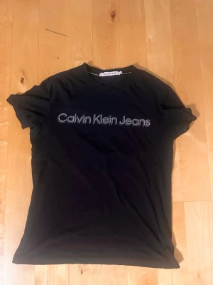 Svart Calvin Klein Jeans t-shirt - Snygg svart t-shirt från Calvin Klein Jeans med logga tryckt i vitt på bröstet. Klassisk rund hals och korta ärmar. Tillverkad i mjuk bomull som känns skön mot huden. Perfekt till jeans eller shorts för en clean och enkel look.