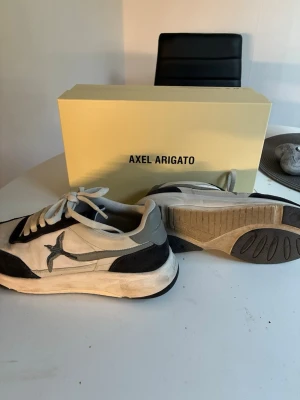 Axel Arigato Sneakers - Snygga sneakers från Axel Arigato i svart och vitt med grå detaljer. Skorna har en chunky sula och klassisk låg silhuett. Tillverkade i en mix av mocka och textil med snörning framtill och logga på sidan. Perfekta för dig som gillar stilrena och trendiga sneakers. De är i mycket bra skick utöver att de är smutsiga, som lätt bara går att tvätta. Tar emot byten också!