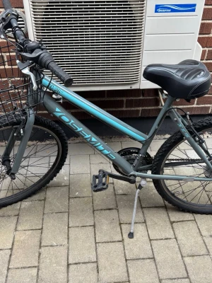 Grå Yosemite cykel med korg - Säljer en fin och välskött Yosemite XC 26” i snygg grå/turkos färg. Cykeln är bekväm att cykla på och passar perfekt för både vardag, skola och fritid. Den har 6 växlar, en stor och praktisk framkorg, bekväm sadel och stöd. Däcken har bra grepp och fungerar lika bra på asfalt som grusvägar. Cykeln är i bra skick med normalt bruksslitage och fungerar som den ska – det är bara att hoppa upp och cykla! Hör gärna av dig om du har några frågor.