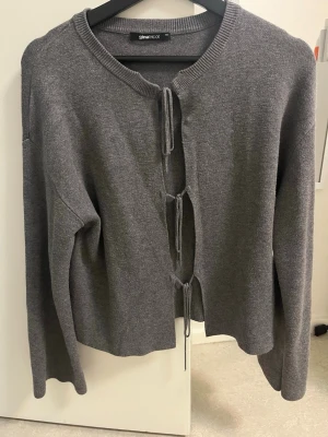 Grå stickad kofta från Gina Tricot - Trendig grå stickad kofta från Gina Tricot med tre knytband framtill. 