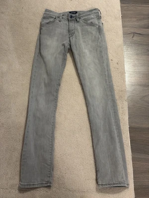 Ljusgrå slim fit jeans - Säljer ett par ljusgrå slim fit jeans med klassisk femficksdesign och dragkedjegylf. Jeansen har raka ben och subtila slitningar för en avslappnad look. Perfekta till sneakers eller boots och passar till många olika stilar.