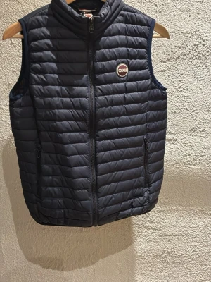 Mörkblå dunväst från Colmar - Snygg mörkblå dunväst från Colmar med quiltad design och hög krage. Västen har dragkedja framtill, två sidofickor med dragkedja och Colmar-logga på bröstet. Perfekt för lager-på-lager och ger en sportig look. Nu pris 2500 kr ungefär. Hör av er vid frågor. Pris kan diskuteras 😃