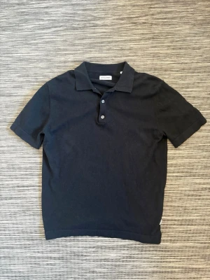 Svart piké från Jack & Jones - Klassisk svart pikétröja från Jack&Jones med korta ärmar, krage och knappar framtill. Tillverkad i mjuk bomull som känns skön mot huden. Enkel och stilren design som funkar till det mesta.