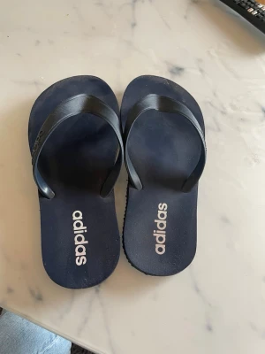 Marinblå flip-flops från Adidas - Säljer dessa adidas flipflops då de inte används längre, användes en vecka utomlands , sedan inget mer🤩