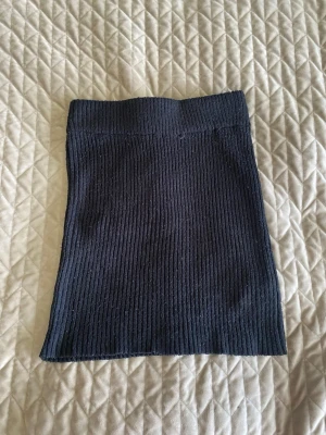 Svart ribbad/stickad kortkjol - Säljer en svart ribbad/stickad kortkjol i stretchigt material. Kjolen har en enkel och stilren design med hög midja och smal passform. Går dock att vika ned till lågmidjad. Perfekt att matcha med en crop top eller oversized tröja för en trendig look. Lite nopprig men inget jag själv  tänker på!