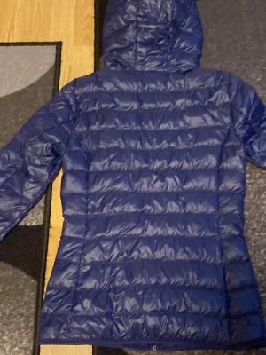 Blå dunjacka från EA7 Emporio Armani - Snygg blå dunjacka från EA7 Emporio Armani med huva och dragkedja framtill. Jackan har ett quiltat mönster och logga på bröstet. Perfekt inför hösten. Och jag säljer endast för 500kr