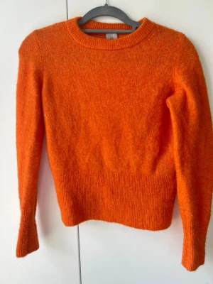 Orange stickad tröja i alpacka från H&M - Säljer en snygg orange stickad alpacka tröja från H&M i storlek XS. Tröjan har rund halsringning, långa ärmar och ribbade muddar vid ärmslut och nederkant. Perfekt för dig som vill ha en färgklick i garderoben!