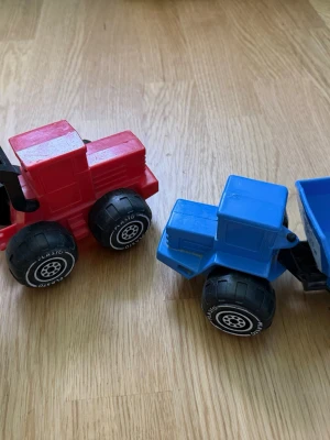 Plasto leksakstraktorer röd & blå - Två färgglada leksakstraktorer från Plasto, en röd och en blå. Tillverkade i tålig plast med stora svarta hjul och vita detaljer. Perfekta för lek på golvet eller i sandlådan. Säljes tillsammans.