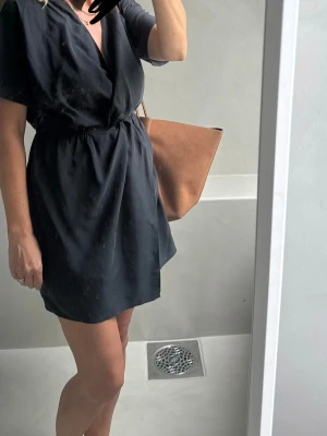 Svart klänning från & Other Stories - Stilren svart kortklänning från & Other Stories med v-ringning. Klänningen har korta ärmar och resår i midjan för en snygg passform. Perfekt för dig som gillar enkel men chic stil.