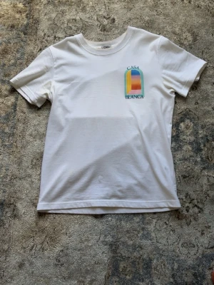 Vit Casa Blanca t-shirt med tryck - Snygg vit t-shirt från Casa Blanca med färgglatt grafiskt tryck fram och stort tryck på ryggen. T-shirten har rund hals och korta ärmar. Perfekt för dig som gillar stilrena plagg med en twist.