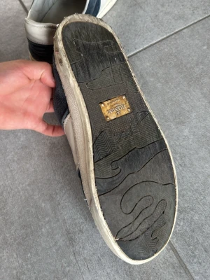 Valentino vita och svarta sneakers - Snygga sneakers från Valentino i vitt och svart läder med detaljer i mocka. Skorna har en klassisk låg siluett och robust gummisula med Valentino-logga undertill. Tillverkade i Italien för en exklusiv känsla och stil. Obs kommer inte med box 