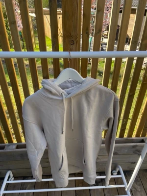 Beige hoodie med ficka framtill - Snygg beige hoodie med huva och dragsko, samt en stor känguruficka framtill. Hoodien har en avslappnad passform och ribbade muddar vid ärmslut och nederkant. Perfekt för en chill och stilren look. Den är från HM och storlek EU XS. Helt nytt skick