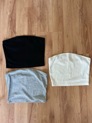 3-pack ribbade tubtoppar från SHEIN - Säljer ett 3-pack bandeau tubtoppar från SHEIN i svart, vit och ljusgrå. Alla topparna är ribbade och ärmlösa, perfekta att styla till olika outfits. Materialet är mjukt och stretchigt, vilket gör dem bekväma att bära hela dagen.