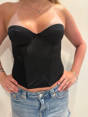 Svart axelbandslös korsett  - Snygg svart korsett i satin material. Passar perfekt till festliga tillfällen. 