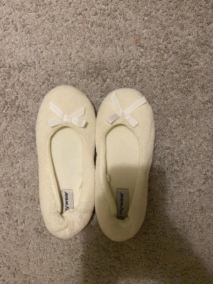 Vita fluffiga tofflor med rosett - Mysiga vita tofflor från mywear i mjukt och fluffigt material. Ballerinamodell med söt liten rosett framtill. Perfekta att glida runt i hemma för en chill vibe. Passar för storlek 36/37