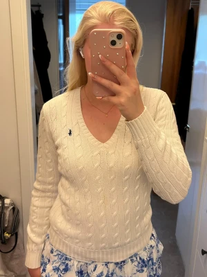  kabelstickad Ralph Lauren - Kabelstickad vit tröja från Ralph Lauren med V-ringning och lång ärm. Har en svag gulaktig fläk på magen men upplever inte att den syns om man inte tittar väldigt noga. 