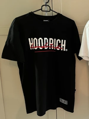 Svart Hoodrich t-shirt med tryck - Snygg svart t-shirt från Hoodrich med stort vitt och rött tryck på både fram- och baksidan. Klassisk rund hals och korta ärmar. T-shirten har en streetwear vibe och är tillverkad i mjuk bomull för skön komfort.