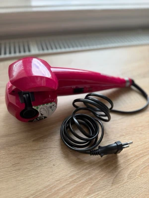 BaByliss rosa automatisk locktång Secret - En rosa automatisk locktång från BaByliss. Verktyget är gjort i plast och metall och har en modern, ergonomisk form. Perfekt för att fixa snygga lockar snabbt och enkelt. 