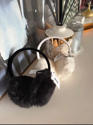 Fluffiga öronmuffar i svart och vitt - Två par öronmuffar i mjuk, fluffig fuskpäls – ett par svarta och ett par vita. Perfekta för att hålla öronen varma under kalla dagar. Båda har en enkel, rund form och breda band. Märke: Bik Bok. Båda för 200kr, orginalpris 179 för 1st