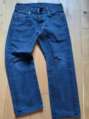 Levi's jeans w30 - Klassiska blå jeans från Levi's med rak passform och fem fickor. Jeansen har en djupblå tvätt, knappgylf och detaljer i kopparfärg. Tillverkade i slitstark denim som ger en tidlös look. Perfekta för dig som gillar en enkel och clean stil.