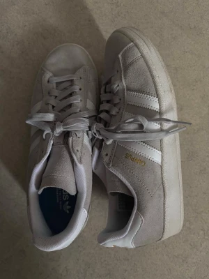 Adidas Campus grå sneakers - Snygga Adidas Campus sneakers i ljusgrå mocka med klassiska vita ränder på sidorna och guldfärgad text. Använt 3-4 gånger. 🌸